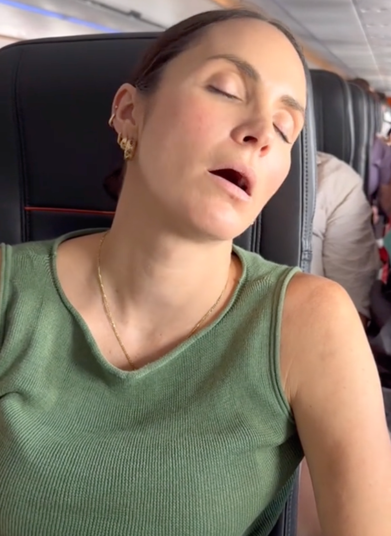 Passenger sleeping sideways in an airplane seat with head tilted and unsupported, illustrating the difficulty of side sleeping on planes